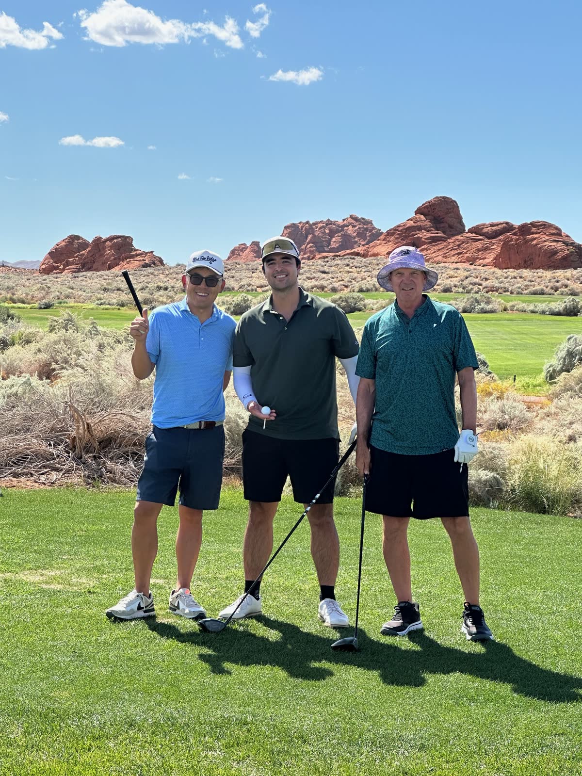 Three golfers on the tee at Sand Hollow with red-rock formations behind